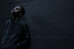 man wearing black button-up jacket standing and leaning against the wall while looking up